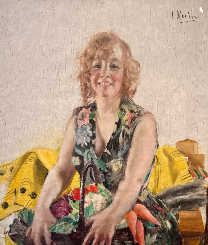 Ingrid Linnea Ruinin maalaus naisesta keittiössä, kukkamekko ja vihanneksia sylissä, kotipuutarhan antimet esillä