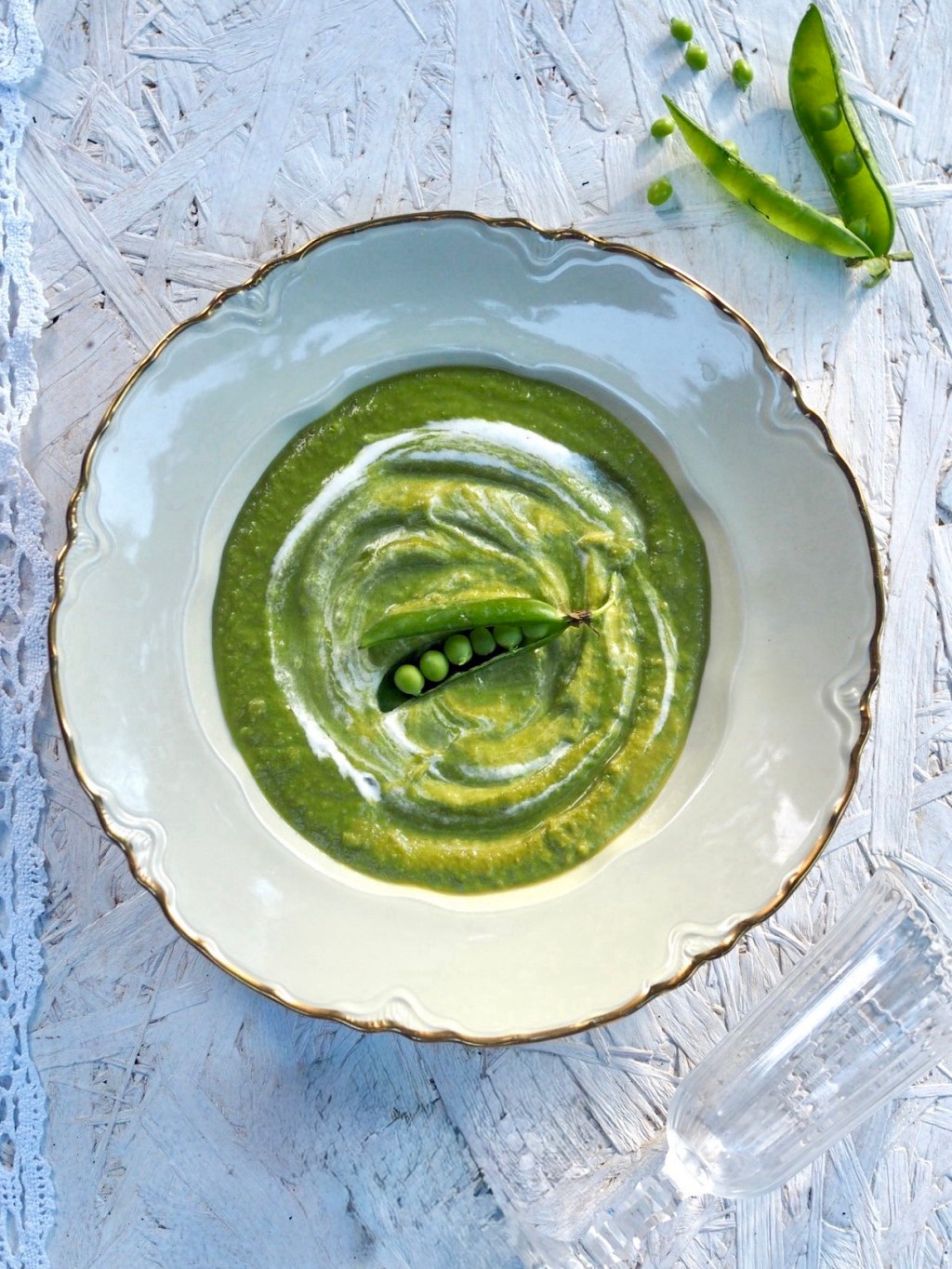 Samettinen tuorehernekeitto kulhossa, koristeltuna kermalla ja tuoreilla herneillä, keväinen alkuruoka.