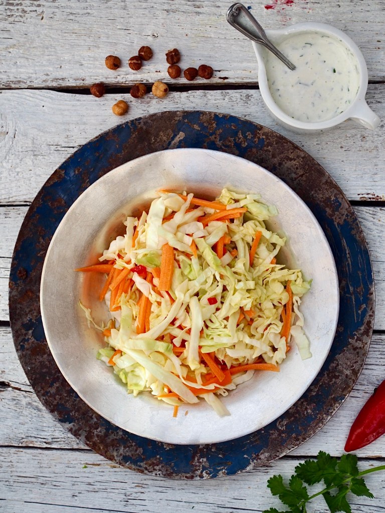 Aasialainen varhaiskaalisalaatti kulhossa, valmistettuna varhaiskaalista, porkkanasta ja chilistä, vierellä kastikekannu.